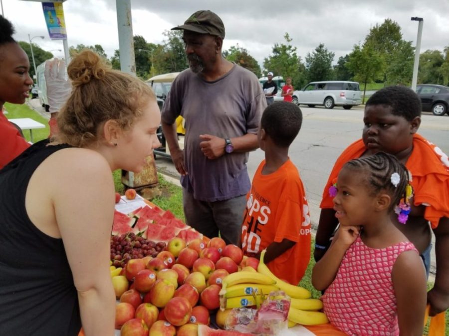 An adult talking to children in front of a fruit stand.